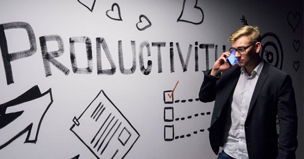 Recruiter on a phone in front of a sign on a wall that says "Productivity"